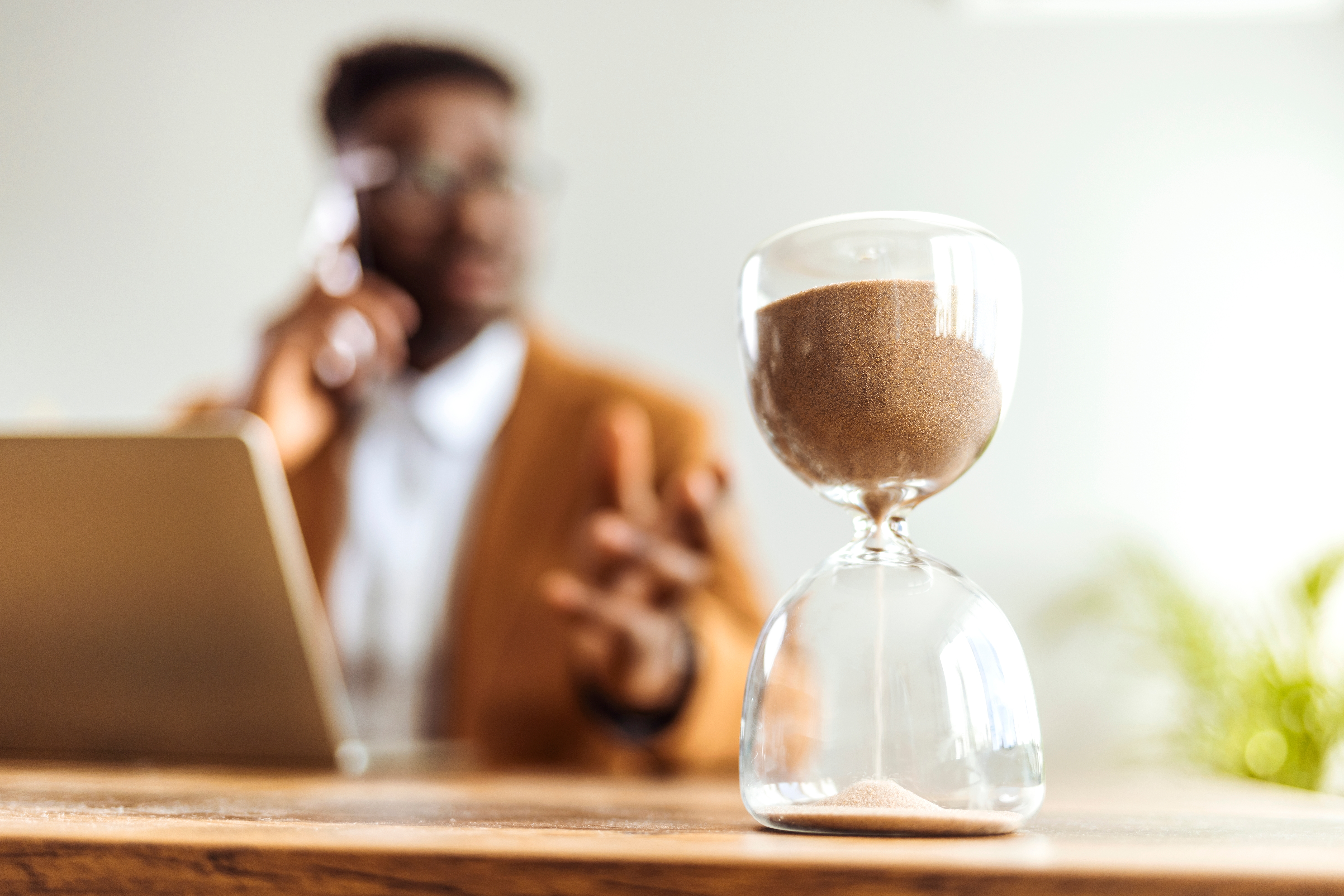 Businessman speak on phone in background, in foreground and focus there is a sand timer