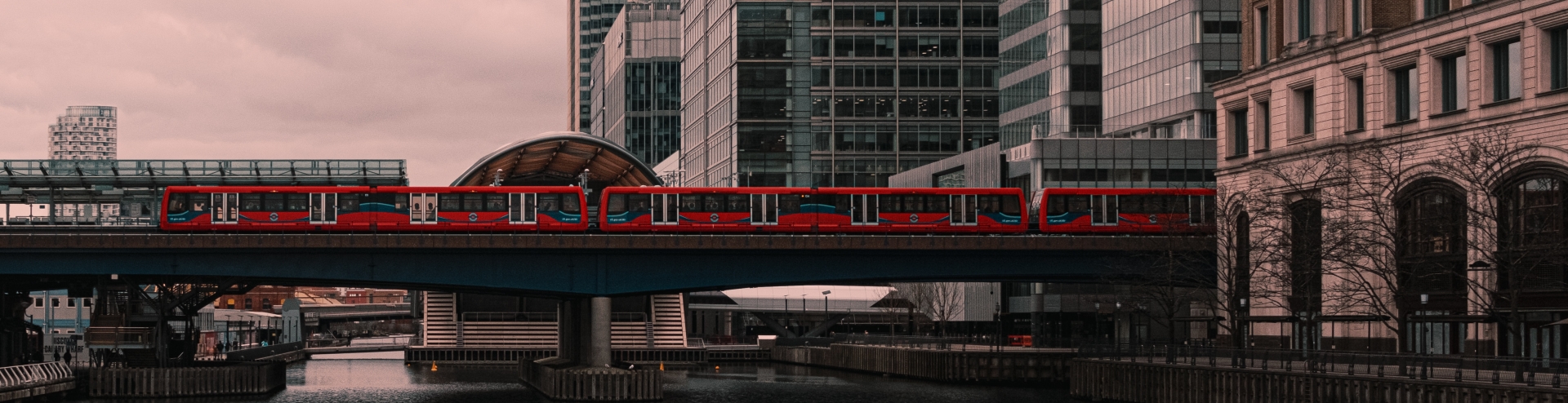 Red DLR train crossing bridge in Canary Wharf in moody light