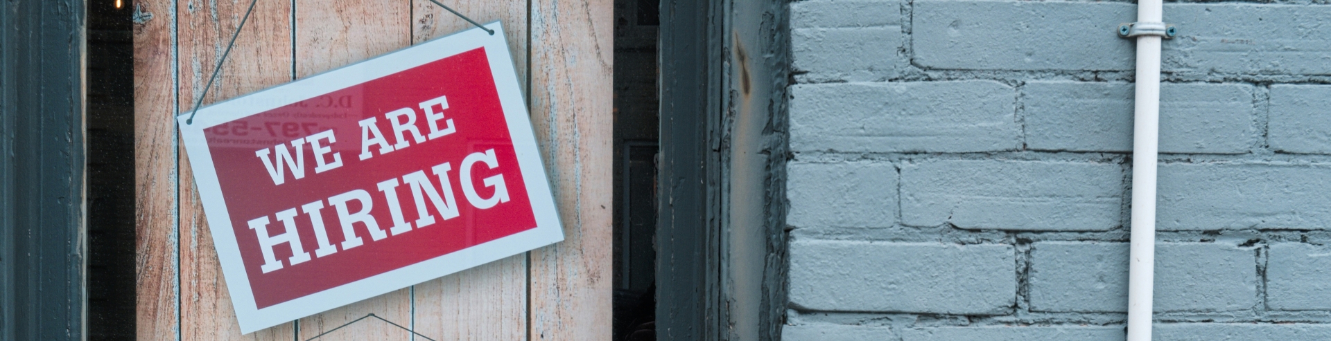 signs hanging off door, signs say 'we are hiring, apply today'