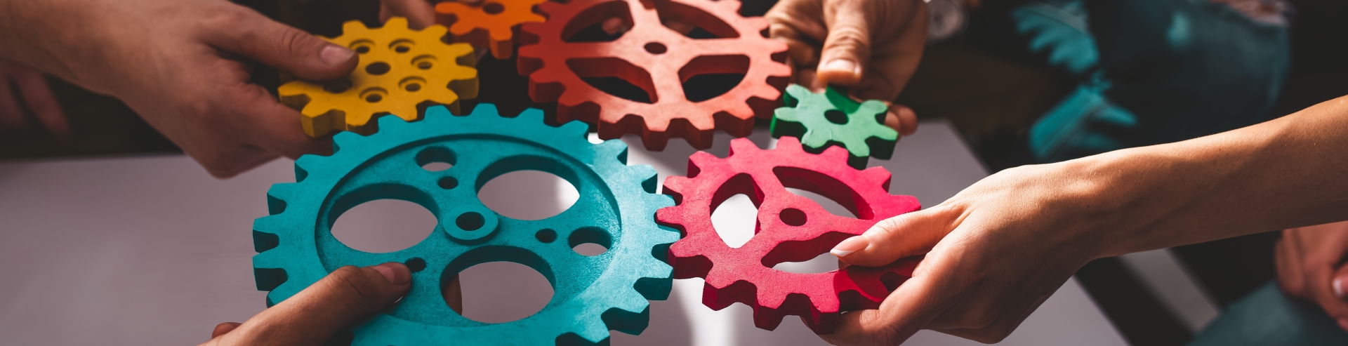 Many colourful cogs being held together by the hands of different people