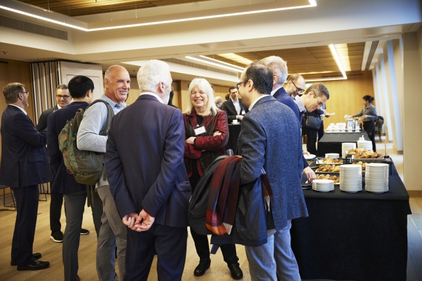 Catering room, group of five people, a female economist and 4 men, discussing, smiling