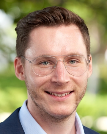 Profile photo of Dr Constantin Charles, white caucasian male, dark blond hair with blue eyes and wearing light coloured frames